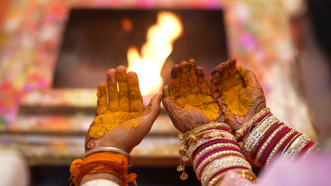 Hands dusted with turmeric held open before a sacred fire