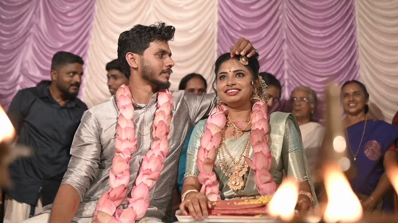 A bride and groom in rose garlands, laughing, the family behind them