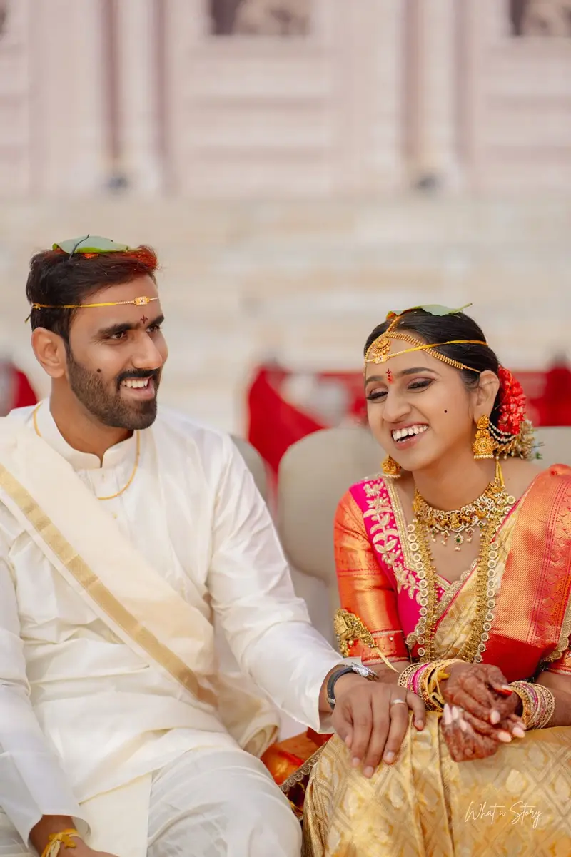 groom in white and bride in yellow-gold silk laughing, seated