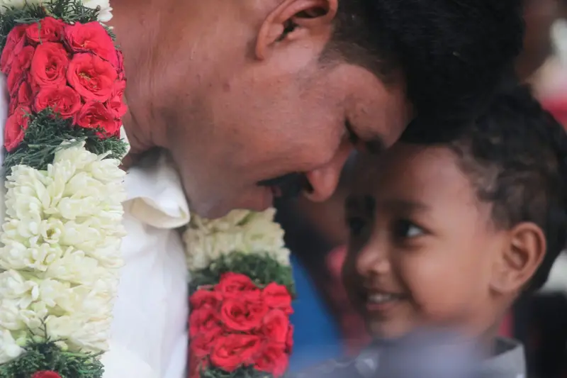 A father and child, faces close, garland; tender.