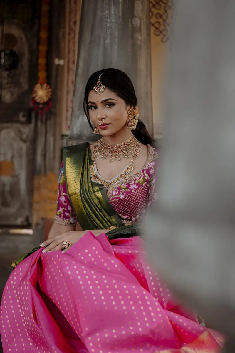 A young woman in a pink-gold langa voni beside a pillar.