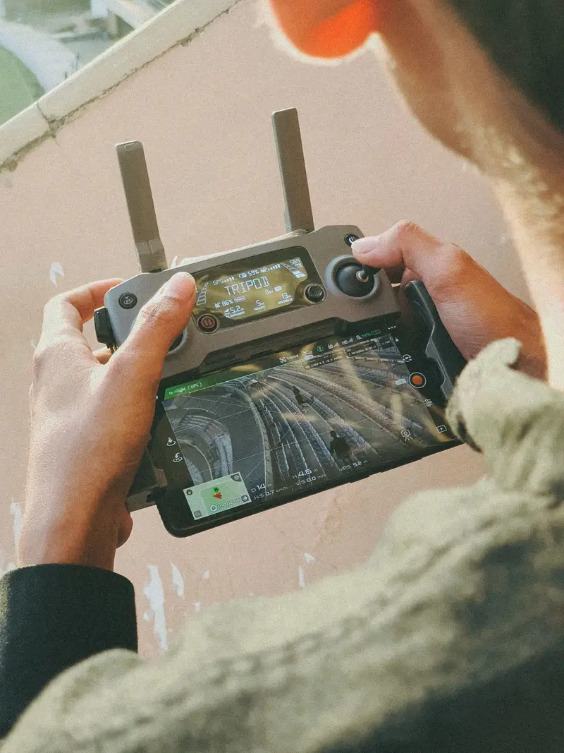 Hands holding a drone controller, its screen showing a live view from above