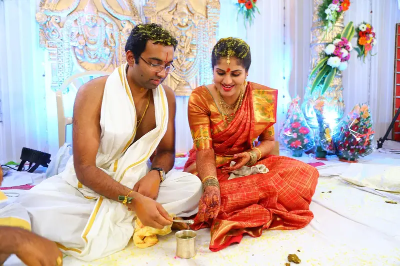 Couple seated at the mandapam performing a rite, white and red.