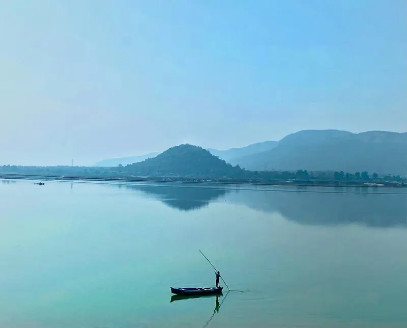A still river with one boat, hills behind it.